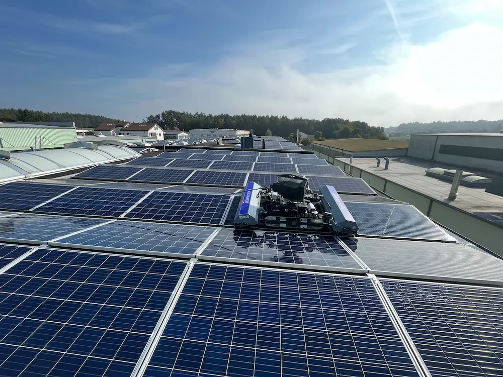 Robosun_Gallery_14 - Robosun Robot cleaning a rooftop solar panel array under a blue sky with sunlight on panels.