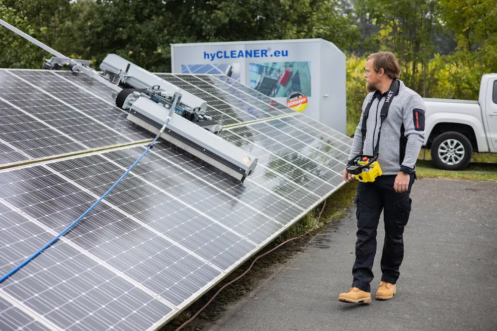 Robosun_Gallery_2 - Robosun Man in protective gear stands beside tilted solar panels, holding a remote controller while a service van labeled hyCLEANER.eu sits in the background.