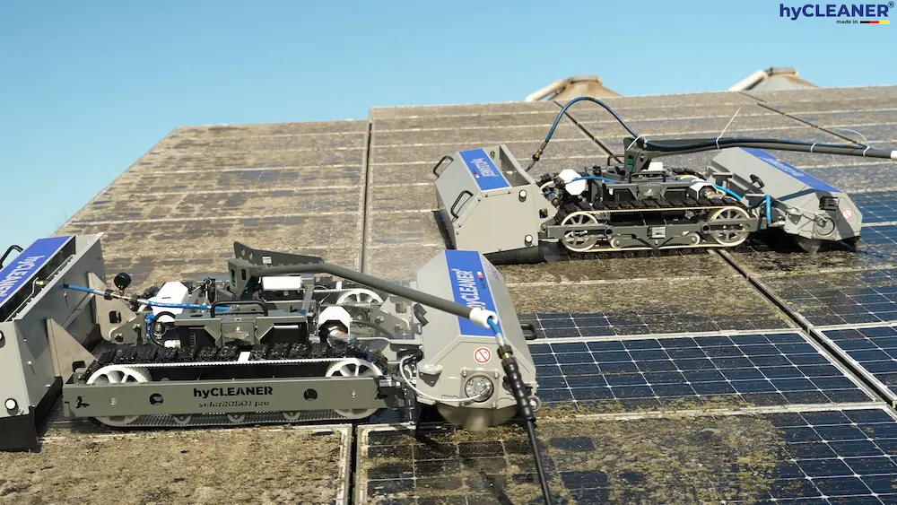 Robosun_Gallery_9 - Robosun Two hyCleaner robotic cleaners moving across solar panels on a rooftop with cables connected to equipment nearby.