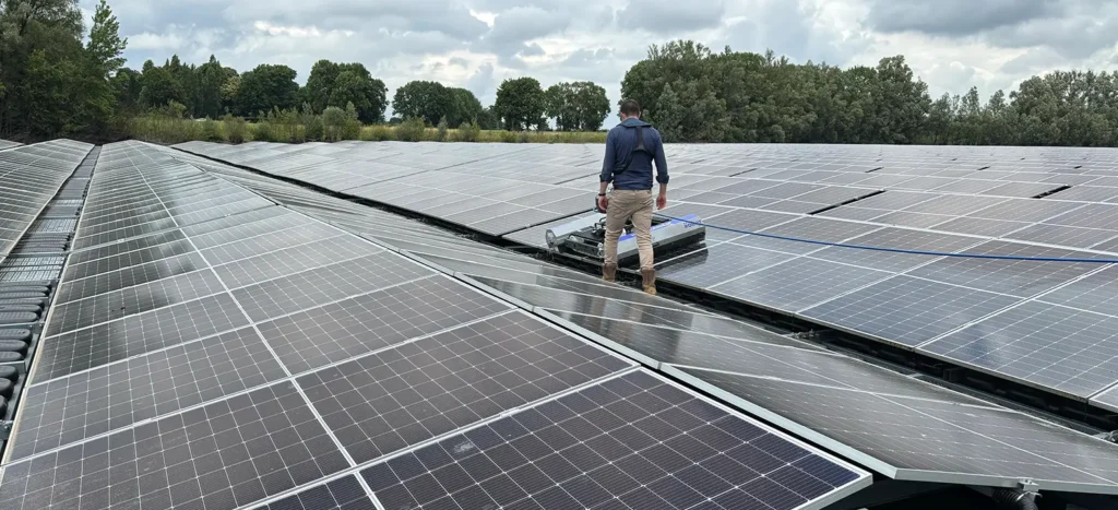 A technician stands between rows of solar panels on a rooftop, inspecting the installation outdoors under a cloudy sky.