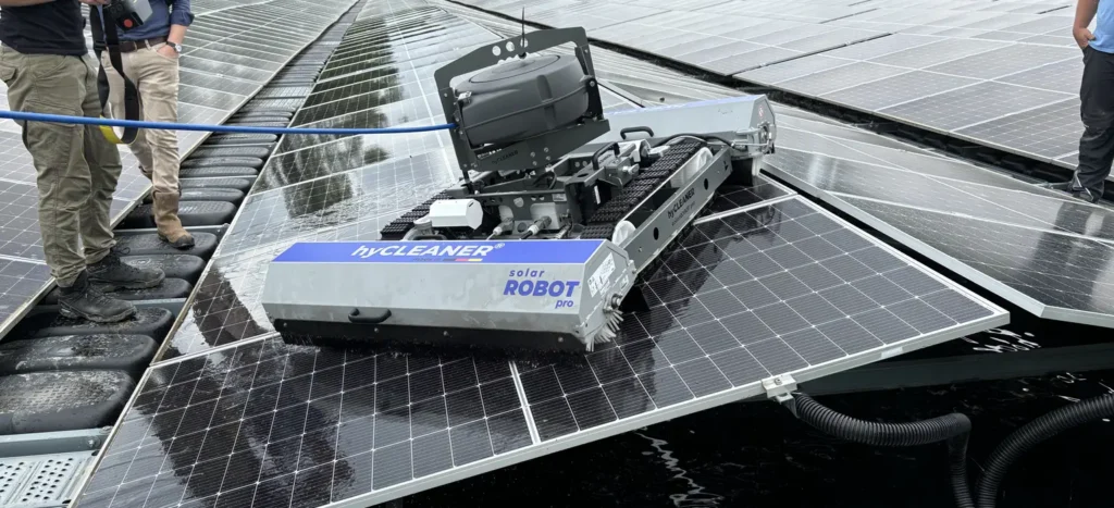 Automated solar-panel cleaning robot operating on tilted photovoltaic panels with technicians nearby in a rooftop setup